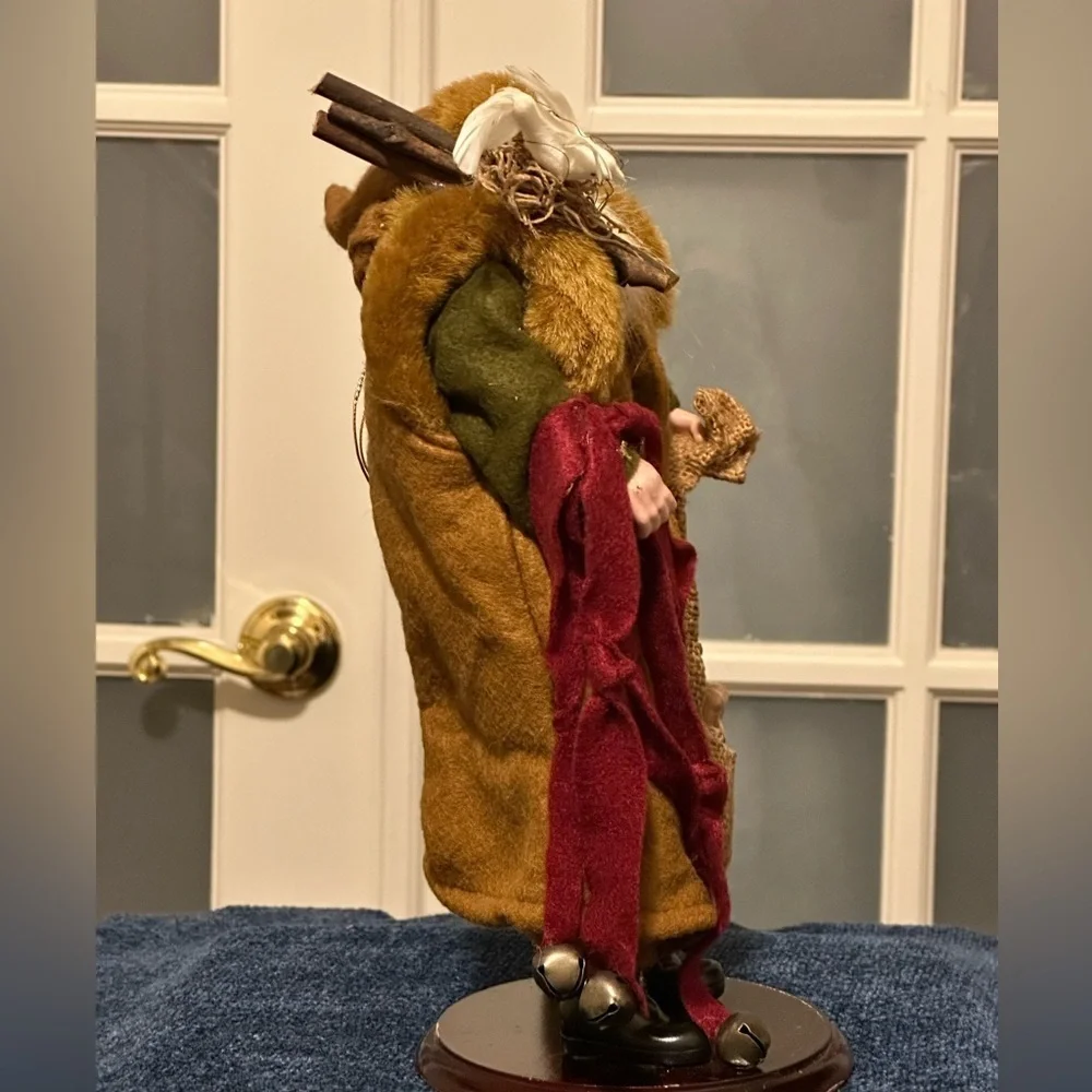 Shaggy haired and bearded Santa wears a brown cape and carries a burlap sack.